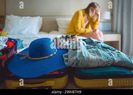 Flugstornierung. Verärgerte Frau, die mit Koffern mit Kleidung auf dem Bett sitzt. Stockfoto