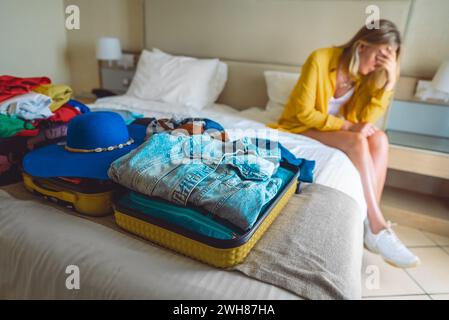 Flugstornierung. Verärgerte Frau, die mit Koffern mit Kleidung auf dem Bett sitzt. Stockfoto