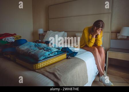 Flugstornierung. Verärgerte Frau, die mit Koffern mit Kleidung auf dem Bett sitzt. Stockfoto