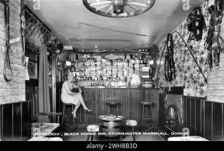 Dorset. Um 1960 – Eine echte Fotopostkarte mit dem Titel „Horsebox, Black Horse Inn, Sturminster Marshall, Dorset“, die die „Horsebox“-Bar im Black Horse Inn zeigt, einem alten kutschenhaus in Sturminster Marshall an der A350 zwischen Poole und Blandford Forum. Die Bar ist mit einer Reihe von Pferdehaltern dekoriert. Die Besitzer John und Jean Sibley sind an der Bar. Stockfoto