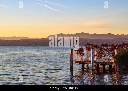 Wunderschöner Blick auf einen Pier in Desenzano del Garda bei Sonnenuntergang. Romantischer Ort und warme Farben für einen romantischen Spaziergang zwischen Liebhabern. Rote Blumen. Stockfoto