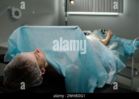 Junge schlafende Patientin unter blauer Abdeckung, die vor der Operation im Krankenhaus im OP vor der Kamera liegt Stockfoto