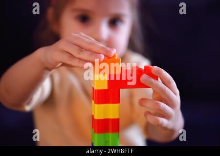 Nahaufnahme eines kleinen Kindes baut einen Turm aus farbigen Plastikblöcken. Das Konzept der Erziehungsspiele und der Kinderentwicklung. Stockfoto