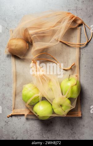 Äpfel und Kiwis in wiederverwendbaren Netzbeuteln. Stockfoto