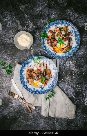 Zwei hübsche antike Teller mit fließenden pochierten Eiern, Schalotten, Pilzen und Speck in Rotweinsauce, auf dunklem Hintergrund Stockfoto