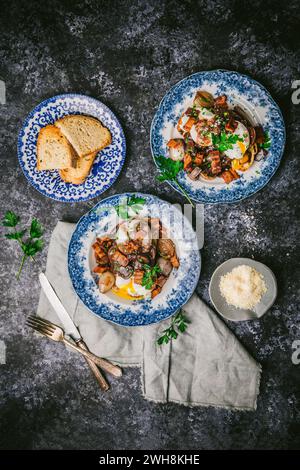 Zwei hübsche antike Teller mit fließenden pochierten Eiern, Schalotten, Pilzen und Speck in Rotweinsauce, mit Teller Toast, auf dunklem Hintergrund Stockfoto