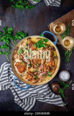 Hühnchen in einer cremigen Weinsauce mit Pilzen, Schalotten und Petersilie in einem blau emaillierten Topf und Serviette Stockfoto