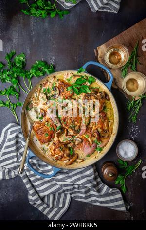 Hühnchen in einer cremigen Weinsauce mit Pilzen, Schalotten und Petersilie in einem blau emaillierten Topf mit Löffel und Serviette Stockfoto