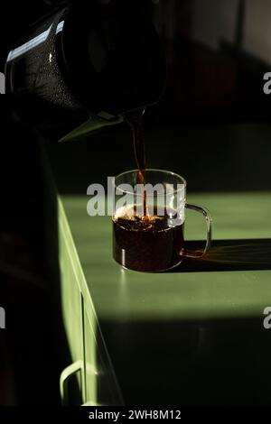 Kaffee wird in eine Glasbecher auf grünem Tisch gegossen. Stockfoto