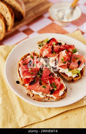 Ricotta- und Parmaschinken-Toast mit Balsamico-Drizzle und Kresse auf gekacheltem Hintergrund Stockfoto