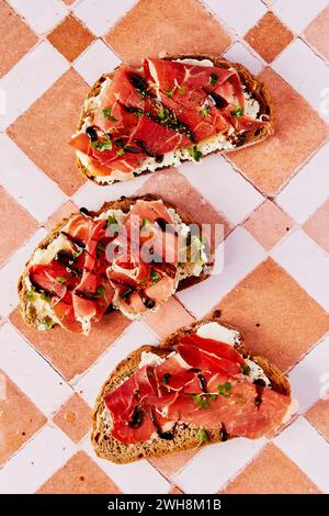 Ricotta- und Parmaschinken-Toast mit Balsamico-Drizzle und Kresse auf gekacheltem Hintergrund Stockfoto