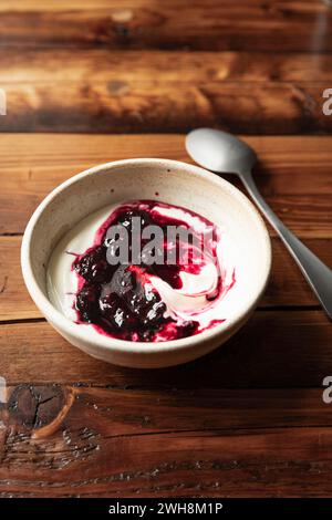 Schüssel mit Joghurt und brombeerkompott auf Holztisch mit Silberlöffel. Stockfoto