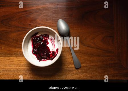 Schüssel mit Joghurt und brombeerkompott auf einem Holztisch mit silbernem Löffel. Stockfoto