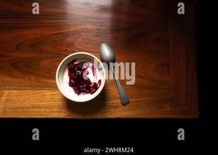 Schüssel mit Joghurt und brombeerkompott auf einem Holztisch mit silbernem Löffel. Stockfoto