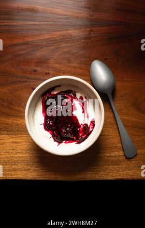 Schüssel mit Joghurt und brombeerkompott auf einem Holztisch mit silbernem Löffel. Stockfoto