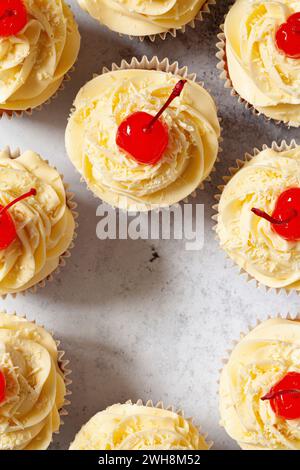 Cupcakes, dekoriert mit Paspelfrosting, geriebener weißer Schokolade und Maraschino-Kirschen mit Stielen. Stockfoto