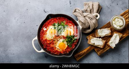 Frühstück Shakshuka gebratene Eier mit Tomaten in der Pfanne und Brot mit weichem Ziegenkäse auf Betonhintergrund Kopierraum Stockfoto