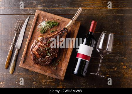 Gegrilltes Tomahawk Steak auf Knochen und Flasche Rotwein auf hölzernem Hintergrund Stockfoto