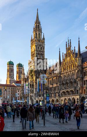 Blick über den Marienplatz in der Münchener Innenstadt während des Sonnenunterganges. Die Sonne scheint auf die Türme des Neugotischen Rathaus mit seinem 85m hohen Turm und im Hintergrund die Frauenkirche, eine gotische Kirche mit dem berühmten Türmen der Münchener Silhouette. Eine der Hauptattraktionen für Touristen in München. München Graggenau Bayern Deutschland *** Blick über den Marienplatz in der Münchner Innenstadt bei Sonnenuntergang scheint die Sonne auf die Türme des neogotischen Rathauses mit seinem 85 m hohen Turm und im Hintergrund auf die Frauenkirche, eine gotische Kirche mit den berühmten Türmen der Stadt Stockfoto