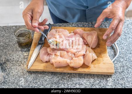 Die Hände eines Mannes, die ein rohes Hühnchen würzen, um es auf einem Schneidebrett zu kochen Stockfoto