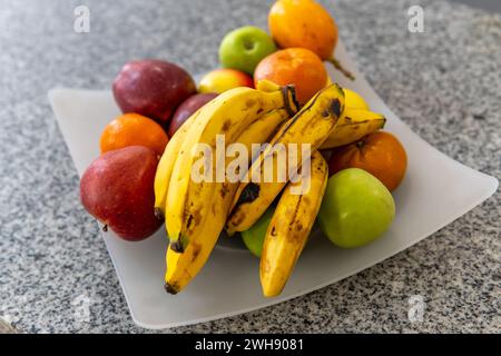 Obstschale mit Bananen, grünen Äpfeln, roten Äpfeln und Mandarinen auf Granitoberfläche Stockfoto