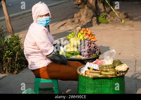 Frau mit Gesichtsmaske, die frisches Obst auf den Straßen von Hanoi, Vietnam, verkauft Stockfoto