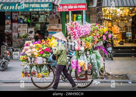 Weibliche Blumenverkäuferin mit einem Fahrrad beladen mit frischen Blumen zum Verkauf, Hanoi, Vietnam Stockfoto