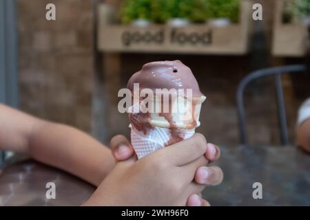 Die Hand eines kleinen Kindes hält eine tropfende Schokoladeneiskegel im Café Stockfoto