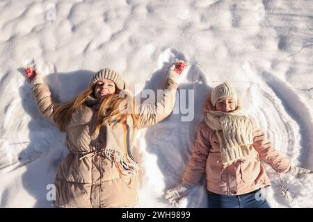 Familienzeit. Glückliche Mutter und ihre Tochter machen Schneeengel am sonnigen Wintertag, über der Aussicht Stockfoto