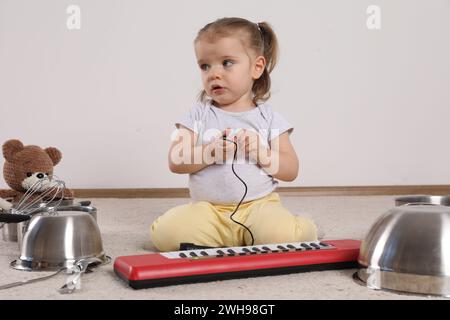 Niedliches kleines Mädchen mit Kochgeschirr und Spielzeugklavier zu Hause Stockfoto