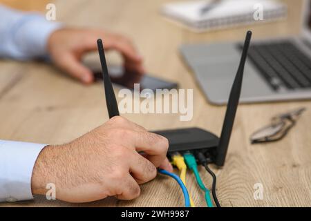 Mann, der Kabel in den WLAN-Router an einem Holztisch drinnen steckt, Nahaufnahme Stockfoto