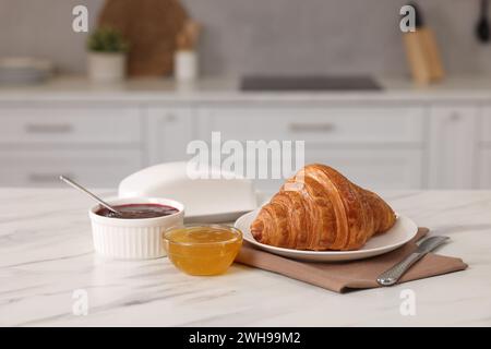 Das Frühstück wird in der Küche serviert. Frisches Croissant, Marmelade und Honig auf weißem Tisch Stockfoto