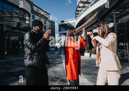 Zwei Geschäftsfrauen, die mit einem männlichen Kollegen an einem sonnigen Tag vor einem modernen städtischen Bürogebäude applaudieren. Stockfoto