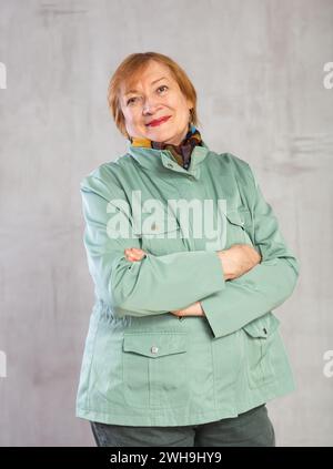 Freundliche Seniorin in hellgrüner Jacke, die mit überkreuzten Armen steht Stockfoto