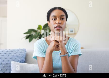Junge birassische Frau sitzt nachdenklich in einem Zuhause bei einem Videoanruf Stockfoto