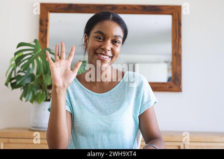 Junge birassische Frau winkt fröhlich in einem Zuhause bei einem Videoanruf Stockfoto