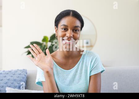 Eine junge, birassische Frau winkt fröhlich aus ihrem Haus bei einem Videoanruf Stockfoto