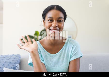 Junge birassische Frau winkt fröhlich bei Videogesprächen, sitzt drinnen Stockfoto