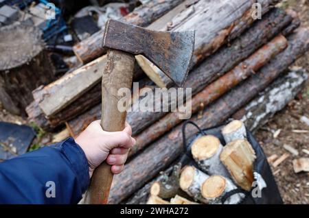 Mann mit Axt. Axt in der Hand. Ein starker Mann hält eine Axt in den Händen vor dem Hintergrund von Feuerholz. Selektiver Fokus, unscharfer Hintergrund Stockfoto