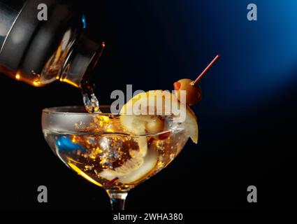 Martini mit grünen Oliven und Zitrone. Der Cocktail wird aus einem Shaker in ein Glas gegossen. Stockfoto