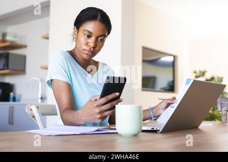 Die junge birassische Frau arbeitet von zu Hause aus und konzentriert sich auf ihr Smartphone Stockfoto