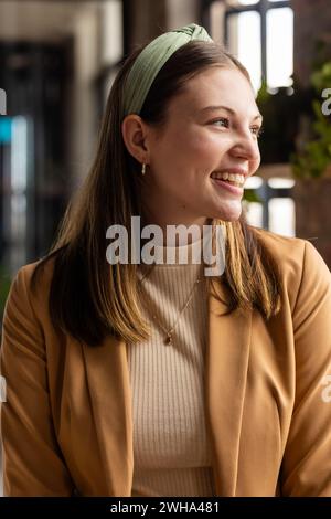 Die junge kaukasische Frau lächelt hell in einem zwanglosen Geschäftsbüro mit Kopierraum Stockfoto