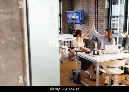 Junge kaukasische Frau und Asiatin feiern Erfolg in einem zwanglosen Geschäftsbüro Stockfoto