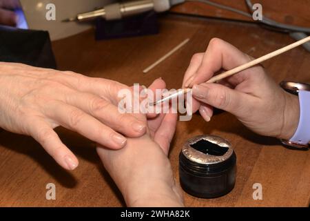 Das Foto zeigt die Hände eines Manikürs und eines Kunden, der mit einem Pinsel Lack auf die Fingernägel aufträgt. Stockfoto