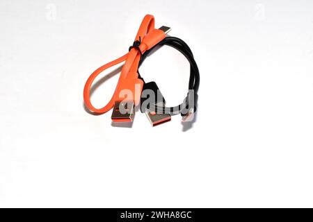 Orangefarbene und schwarze USB-Kabel, die in Ringe verdreht sind, liegen auf weißem Hintergrund. Stockfoto