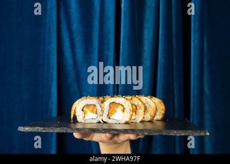 Sushi-Brötchen auf tiefblauem Hintergrund mit blauem Vorhang. Asiatisches Restaurant-Menü-Konzept Stockfoto