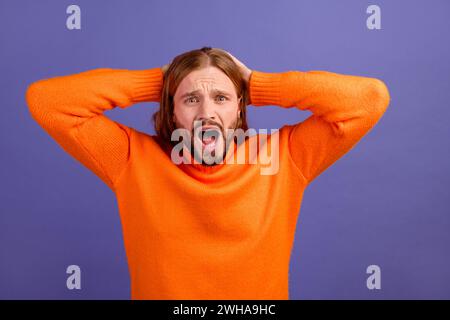 Foto eines jungen lustigen Mannes trägt einen orangefarbenen Pullover, der gestresst ist, als der Boss ihm sagt, dass er das schlechteste Teammitglied ist, das auf violettem Hintergrund isoliert ist Stockfoto