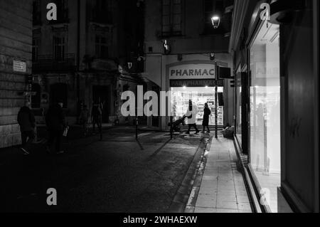 Arles, Frankreich - 7. März 2023: Leere Straße im Zentrum von Arles (Frankreich) in der Nacht, schwarz-weiß, Menschen vor der Apotheke Stockfoto