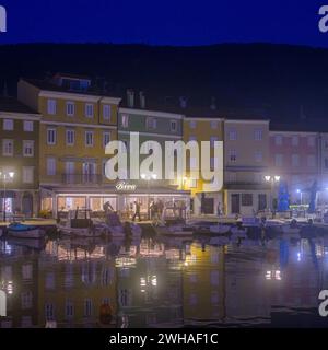 Cres, Kroatien - 24. Oktober 2022: Der Hafen von Cres in der Nacht, nebelige Reflexion von bunten Häusern Stockfoto