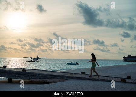 Ein malerischer Blick auf ein Meeresflugzeug am maledivischen Meer, mit einer Frau, die auf dem Dock spaziert, schafft einen idyllischen und ruhigen Küstenort im Paradies Stockfoto
